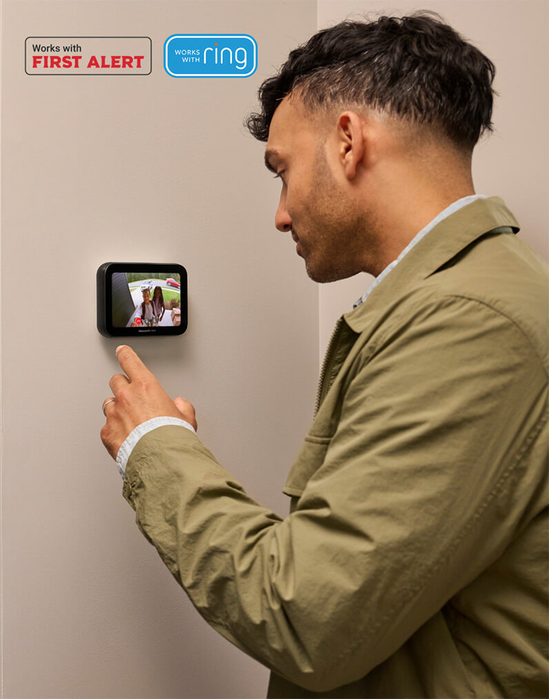 A homeowner is setting up the X8S thermostat on the wall. Honeywell Home X8S Thermostat Works with First Alert and Ring.