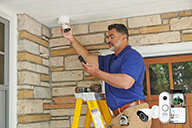  A installer is installing the Resideo Outdoor Camera with the product image in the foreground.