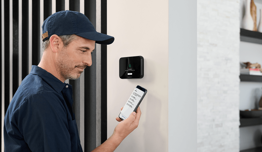 Pro in the home looking at iPhone with ElitePro thermostat in the background.