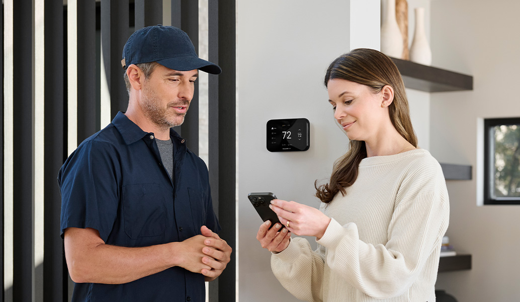 Contractor and homeowner in a home looking at a phone with the  ElitePro Thermostat. 